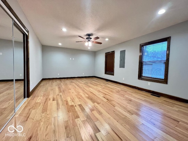 unfurnished bedroom with electric panel, light hardwood / wood-style flooring, ceiling fan, a textured ceiling, and a closet