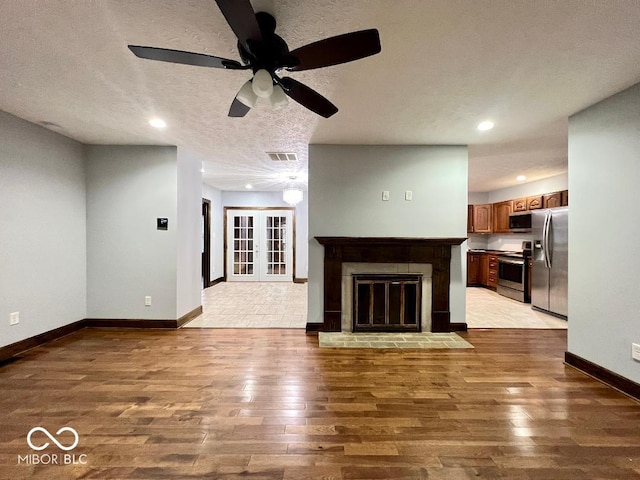 unfurnished living room with ceiling fan, light hardwood / wood-style floors, a textured ceiling, and a brick fireplace