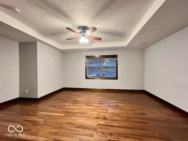 spare room with ceiling fan, wood-type flooring, a textured ceiling, and a tray ceiling