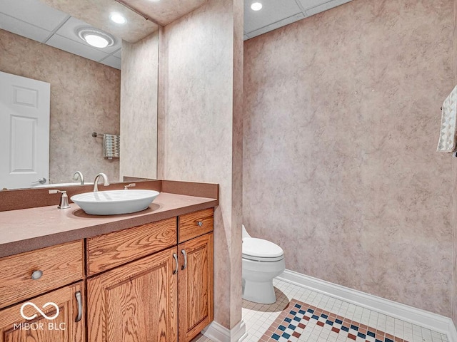 bathroom with tile patterned flooring, a drop ceiling, toilet, and vanity