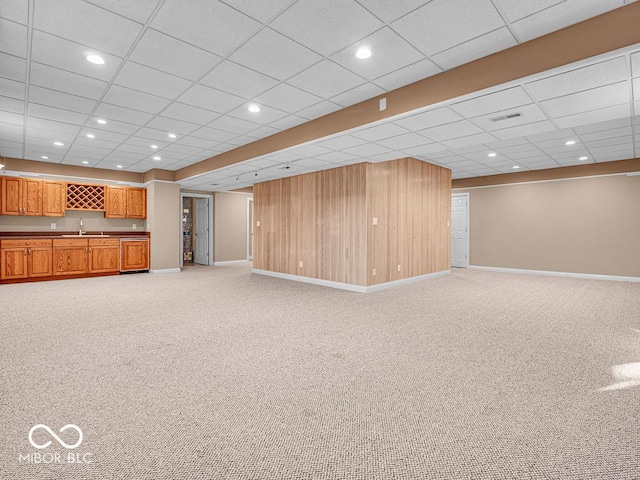 unfurnished living room featuring a paneled ceiling, light carpet, and wood walls