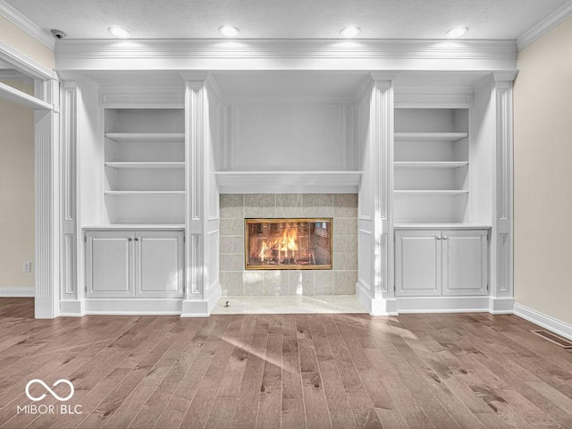 unfurnished living room with a fireplace, crown molding, built in features, and hardwood / wood-style floors