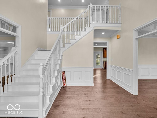 stairs featuring wood-type flooring, a high ceiling, and ornamental molding