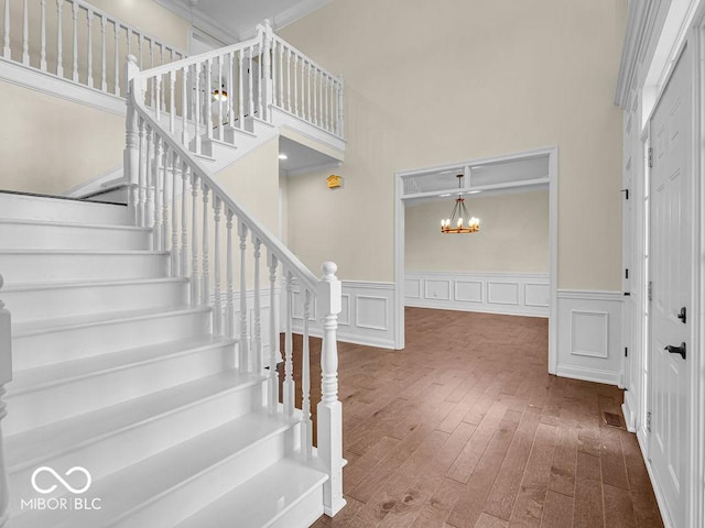 stairway with wood-type flooring, a towering ceiling, crown molding, and a notable chandelier