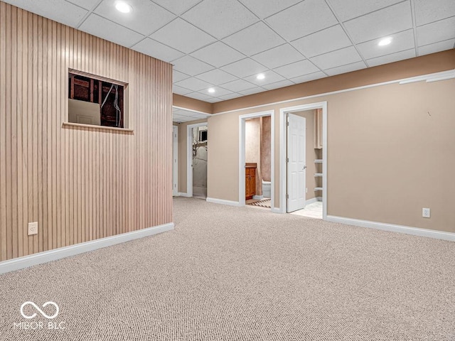 carpeted spare room with a paneled ceiling and wooden walls