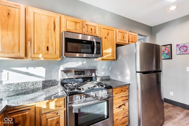 kitchen featuring appliances with stainless steel finishes, light hardwood / wood-style flooring, and dark stone countertops