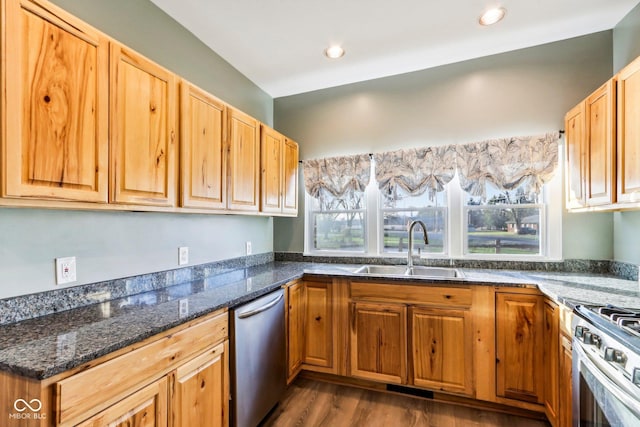 kitchen with appliances with stainless steel finishes, dark wood-type flooring, dark stone counters, and sink