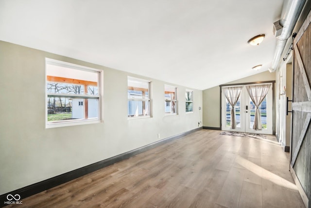 unfurnished room featuring french doors, light wood-type flooring, vaulted ceiling, and a barn door