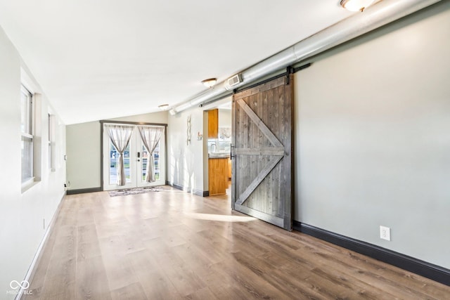 empty room with a barn door, light hardwood / wood-style floors, and lofted ceiling