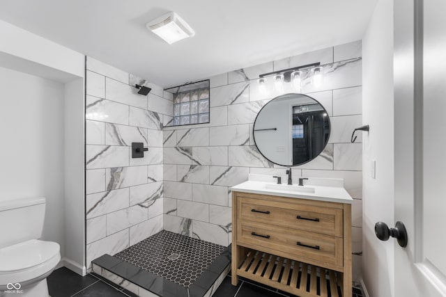 bathroom featuring tile patterned floors, vanity, tiled shower, tile walls, and toilet