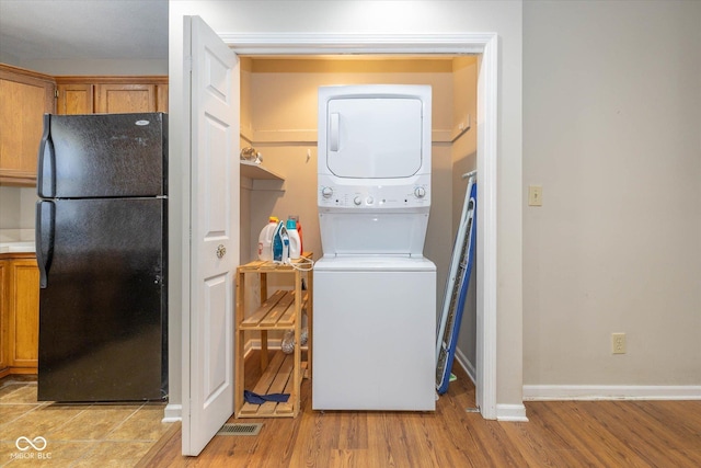 laundry area featuring stacked washer / dryer and light hardwood / wood-style flooring