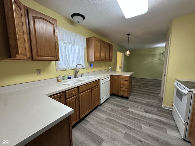 kitchen featuring sink, light hardwood / wood-style flooring, kitchen peninsula, pendant lighting, and white appliances