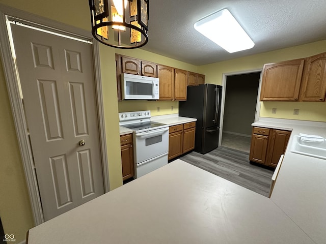 kitchen featuring pendant lighting, white appliances, light hardwood / wood-style flooring, a textured ceiling, and a chandelier