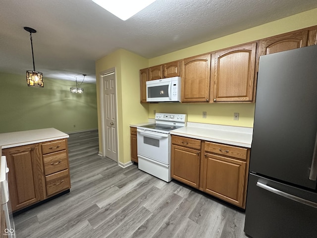 kitchen with a chandelier, a textured ceiling, pendant lighting, light hardwood / wood-style floors, and white appliances