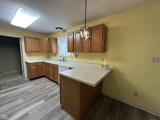 kitchen featuring sink, hanging light fixtures, light hardwood / wood-style flooring, kitchen peninsula, and white dishwasher