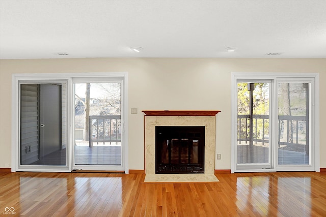 unfurnished living room featuring light hardwood / wood-style flooring, a high end fireplace, and a healthy amount of sunlight