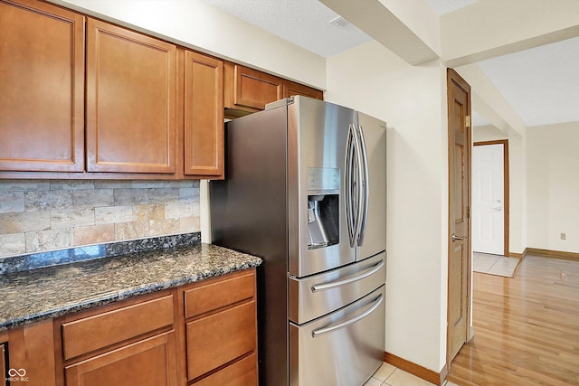 kitchen featuring stainless steel fridge with ice dispenser, light wood-type flooring, tasteful backsplash, and dark stone counters