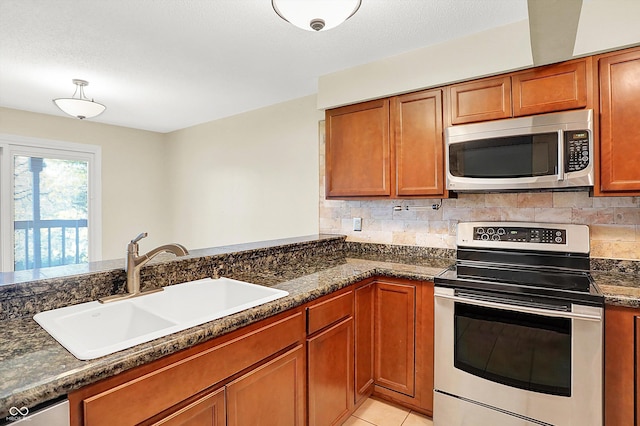 kitchen featuring appliances with stainless steel finishes, tasteful backsplash, sink, light tile patterned floors, and dark stone countertops