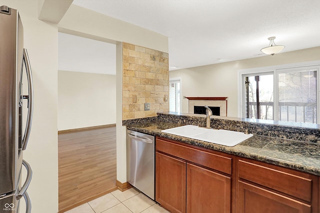 kitchen featuring appliances with stainless steel finishes, dark stone counters, a textured ceiling, sink, and light hardwood / wood-style flooring