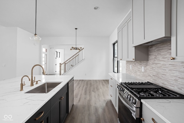 kitchen featuring sink, hanging light fixtures, hardwood / wood-style flooring, light stone countertops, and appliances with stainless steel finishes