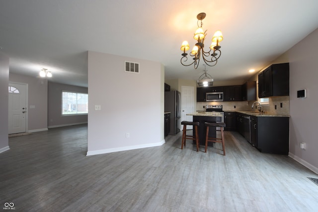 kitchen with sink, decorative backsplash, hanging light fixtures, stainless steel appliances, and light stone countertops