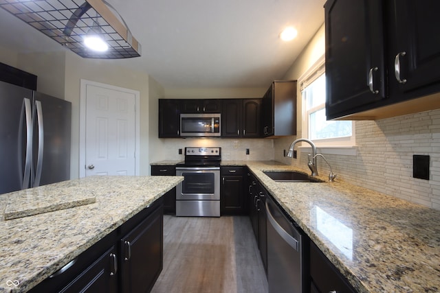 kitchen featuring appliances with stainless steel finishes, hardwood / wood-style floors, tasteful backsplash, sink, and light stone counters