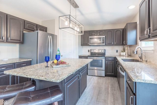 14446 Chapelwood Ln, Fishers, IN 46037 - kitchen with light stone counters, a sink, light wood finished floors, stainless steel appliances, and a kitchen bar