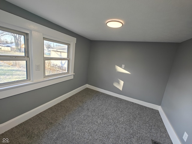 spare room with dark carpet and lofted ceiling