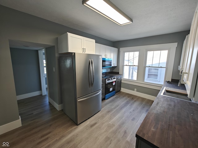 kitchen featuring white cabinets, electric stove, a textured ceiling, light hardwood / wood-style floors, and stainless steel refrigerator