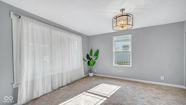 carpeted empty room with an inviting chandelier