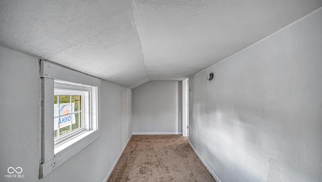 corridor with light colored carpet, lofted ceiling, and a textured ceiling