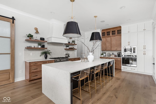 kitchen with a breakfast bar, a center island with sink, a barn door, wood-type flooring, and stainless steel appliances