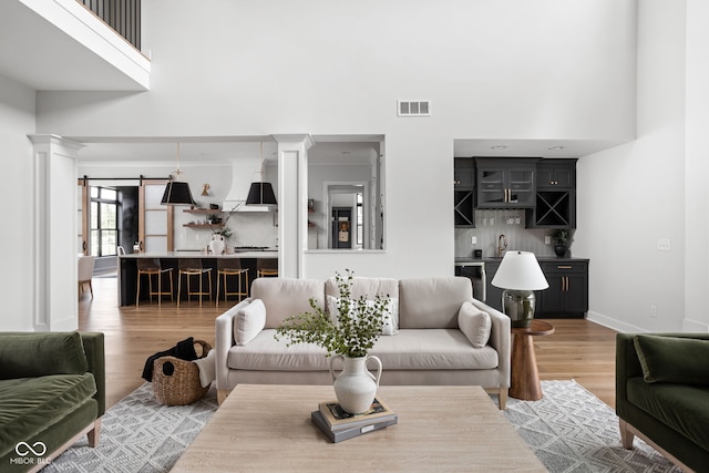 living room with a barn door, wood-type flooring, a high ceiling, and decorative columns