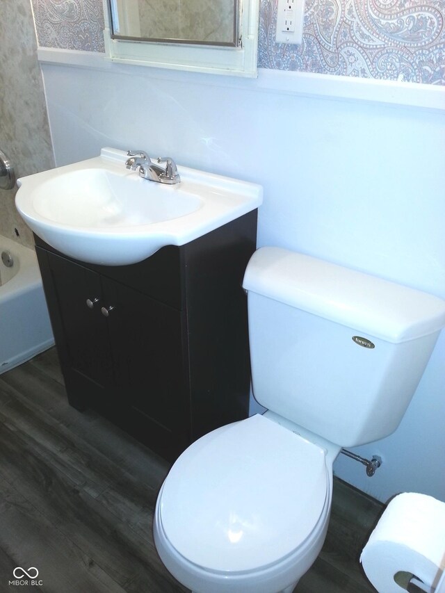 bathroom featuring vanity, a washtub, wood-type flooring, and toilet