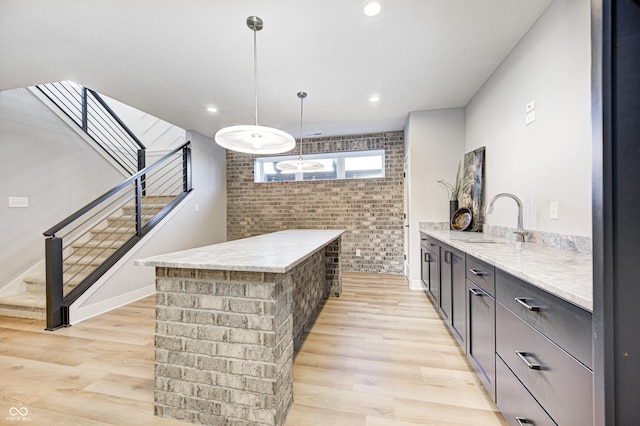 kitchen featuring sink, hanging light fixtures, light stone counters, light hardwood / wood-style flooring, and brick wall