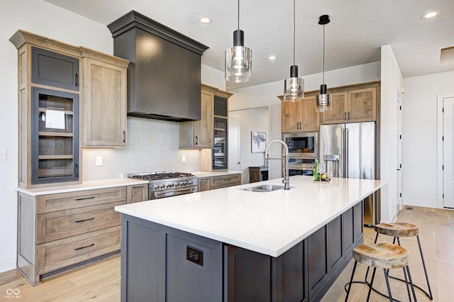 kitchen with sink, wall chimney range hood, premium appliances, an island with sink, and pendant lighting