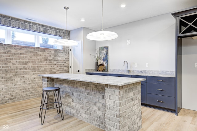 kitchen with a kitchen bar, light stone countertops, light wood-type flooring, brick wall, and decorative light fixtures