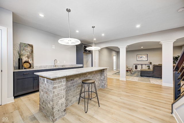 bar with pendant lighting, sink, light stone countertops, light wood-type flooring, and decorative columns