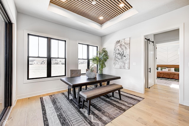 dining area with a barn door, light wood-type flooring, and a tray ceiling