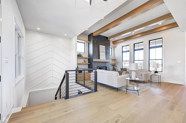 living room with a large fireplace, a healthy amount of sunlight, beam ceiling, and light hardwood / wood-style flooring