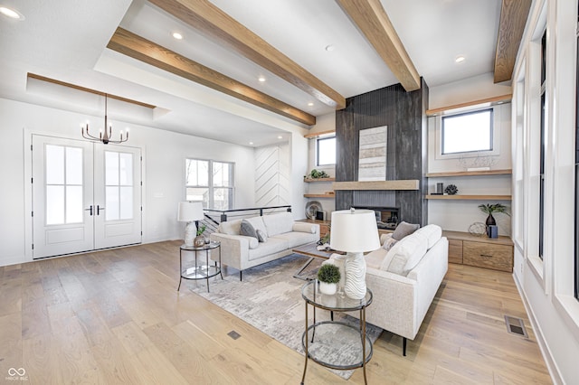 living room with beam ceiling, a large fireplace, a healthy amount of sunlight, and light hardwood / wood-style floors