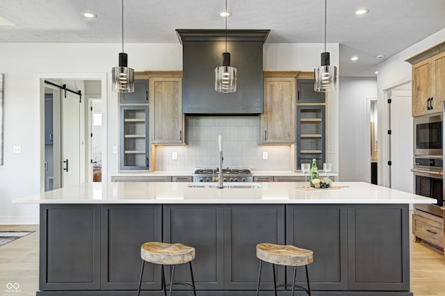 kitchen with a large island, a barn door, pendant lighting, decorative backsplash, and light wood-type flooring