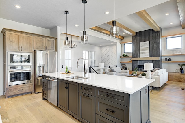 kitchen featuring a kitchen island with sink, sink, light hardwood / wood-style flooring, appliances with stainless steel finishes, and decorative light fixtures