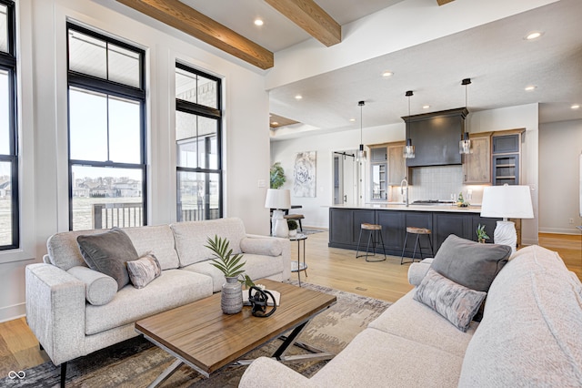 living room with light hardwood / wood-style flooring, beamed ceiling, and sink