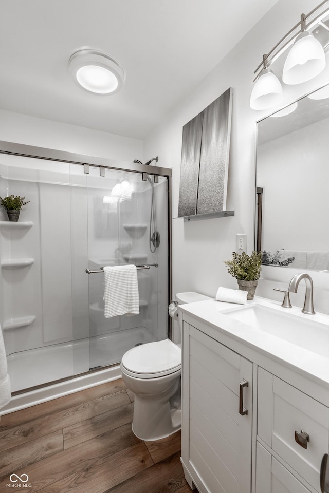 bathroom featuring vanity, toilet, wood-type flooring, and a shower with door