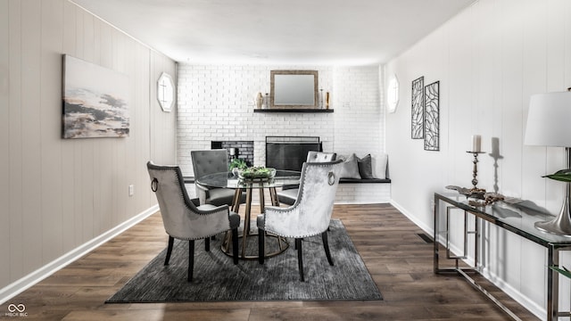 dining area featuring wooden walls, a fireplace, dark wood-type flooring, and brick wall