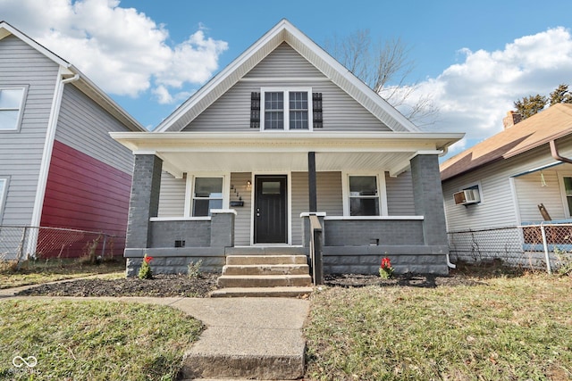 bungalow-style home featuring a front lawn, covered porch, and a wall mounted air conditioner