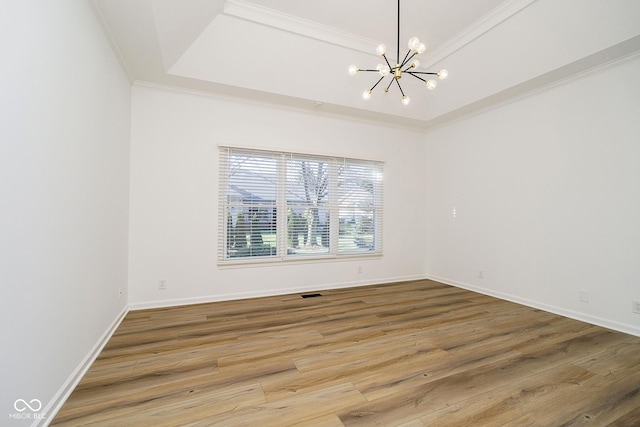 empty room featuring hardwood / wood-style floors, a chandelier, crown molding, and a raised ceiling