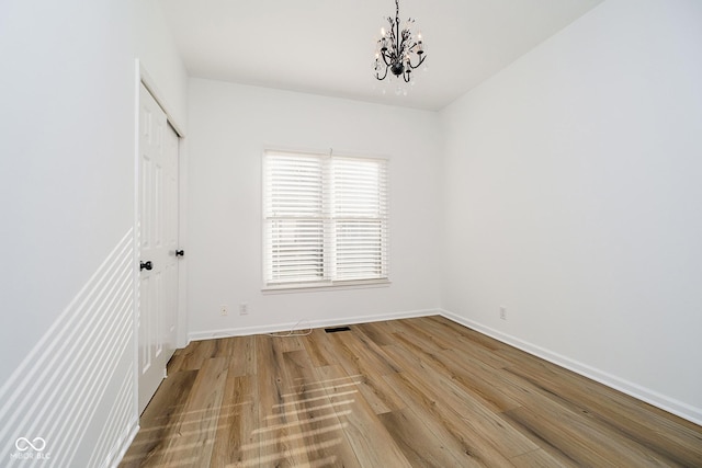 empty room featuring an inviting chandelier and hardwood / wood-style flooring