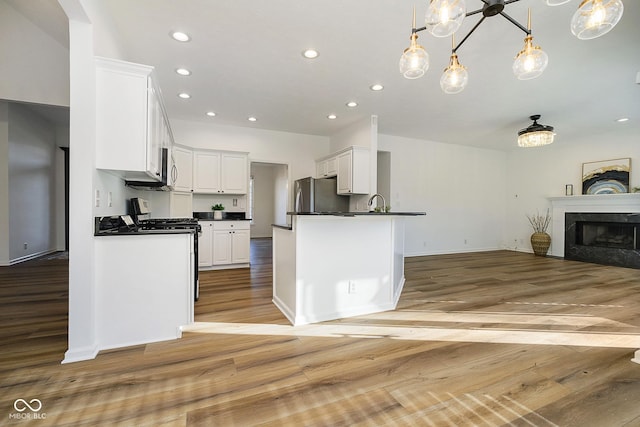 kitchen with white cabinetry, light hardwood / wood-style floors, appliances with stainless steel finishes, a premium fireplace, and pendant lighting